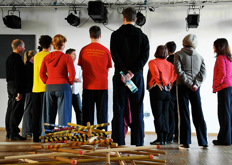 Tschechow-Training: Gruppe lauscht konzentriert dem Dozenten, farbige Stöcke im Vordergrund